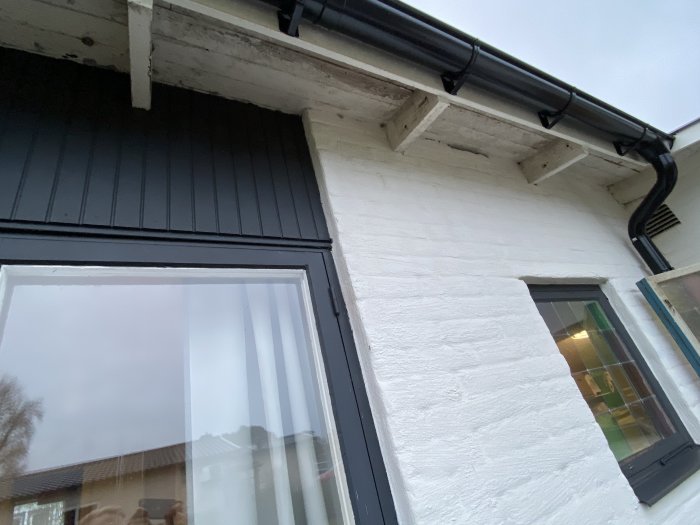 Husfasad med träpanel och vita putsade väggar runt svarta fönster och en dörr.