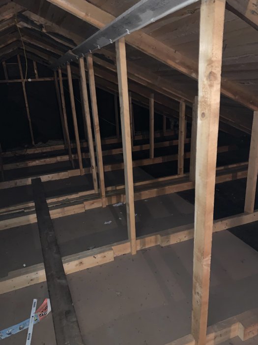 Mörk bild på en vind under renovering med synliga träbjälkar och modulskarvar.