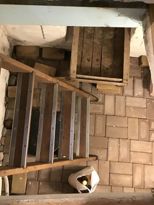 Översikt över en traditionell matkällare med trätrapp och stengolv, synlig isolering och ventilationsöppning.