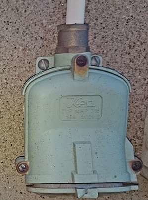 Gammalt SEMKO17 uttag monterat på en vägg med ansluten vit kabel.