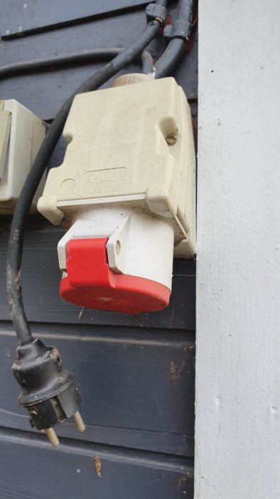 Eluttag monterade på en vägg med en hängande svart stickkontakt.