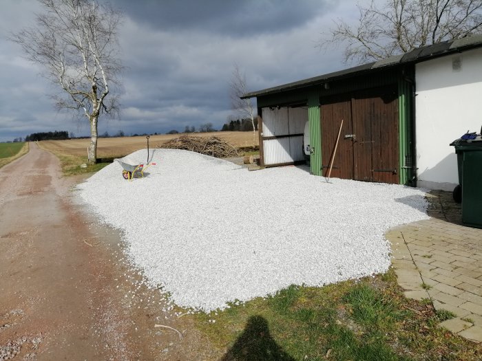 Ny vit makadam på infart framför hus med skottkärra, mot grusväg och garage.