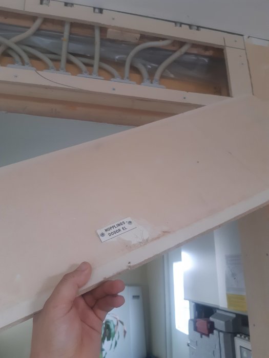 Ett öppet utrymme med synlig kabeldragning och en hand som håller en dörr med en märkskylt märkt "Kopplingsdosor EL".