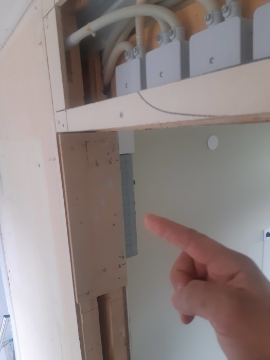 En hand pekar på öppna eldosor i en vägg, med synliga kablar och installationslådor.