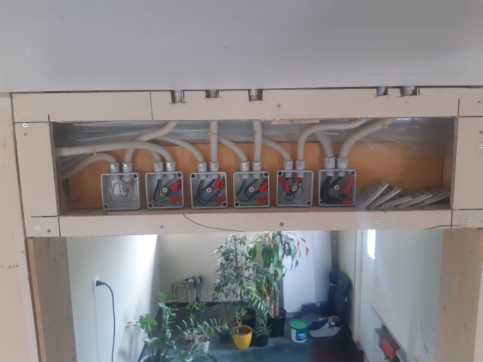 Eluttagsdosor i rad bakom öppen väggpanel med synlig kabeldragning och installationsmaterial.