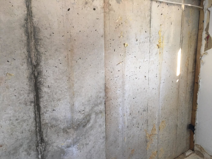 Betongvägg med mögel och fuktskador i källare, synliga isolationsspår och rör.