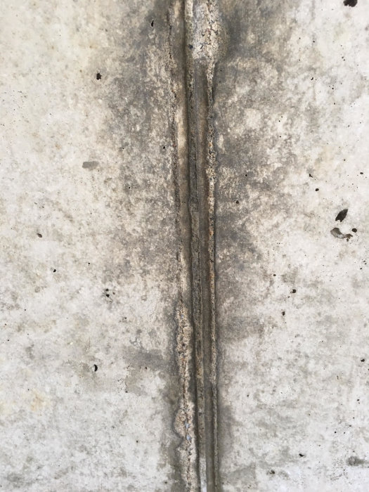 Betongvägg med mögel eller smuts längs en vertikal ränna, frågetecken kring sanering och renovering.