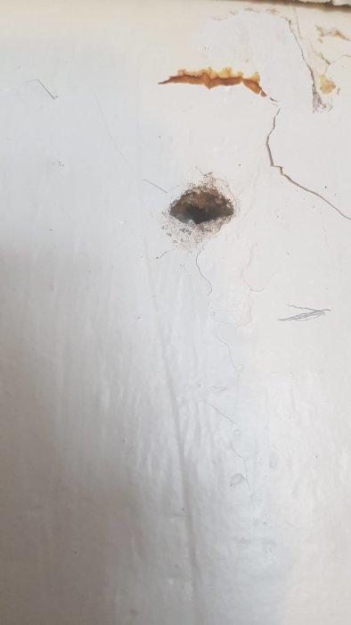 Vägg med förstorat, oregelbundet hål efter borrning där materialet har rasat och ytskiktet är skadat.