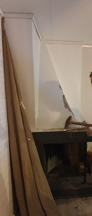 Innanbild på en öppen spis under renovering, med synliga murarbeten och en trave ved bredvid.