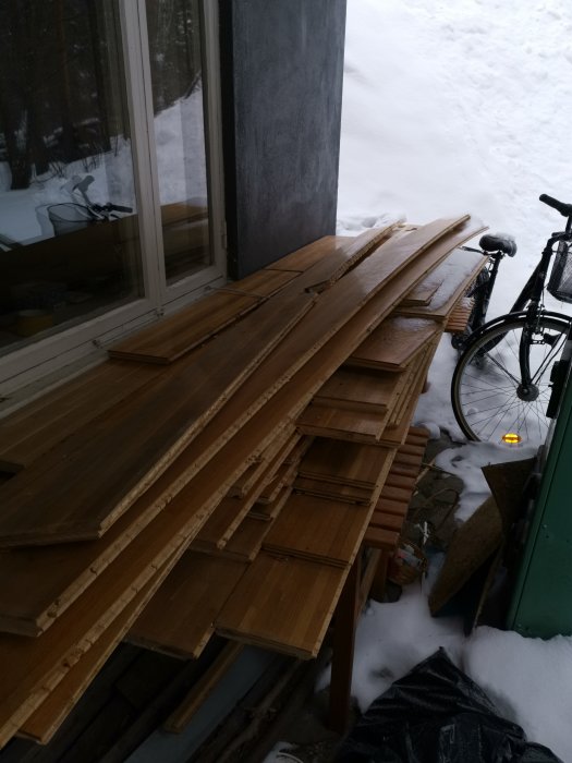 Återvunnet parkettgolv staplat utomhus nära snö och en cykel.