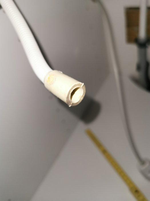 Slutet av en vit torktumlares slang med invändig diameter på cirka 10 mm, med inredningsbakgrund.