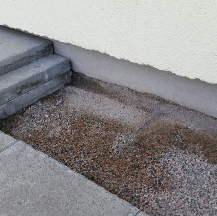 Blöt betonggrund med synliga fuktfläckar nära torra stenplattor och trappsteg vid ett hus.