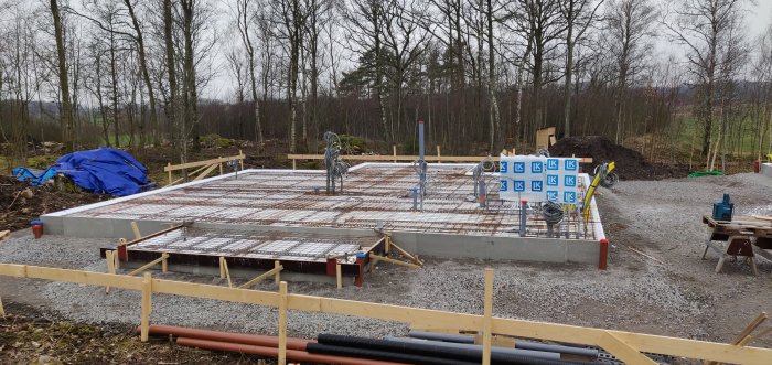 Förberedd betongplatta med armering och elslangar inför gjutning på en byggplats omgiven av träd.