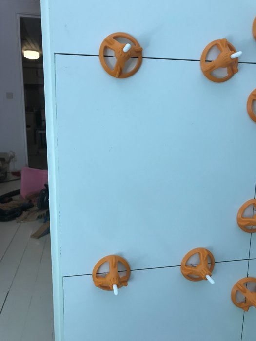 Kakel med nivelleringssystem bestående av orange distanskors och vita kilspetsar under installering.