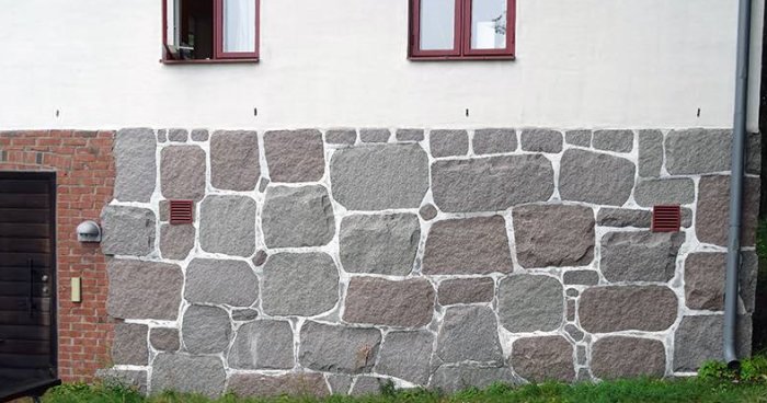 En husvägg med stenbeklädd sockel som ser ut att vara murad med olika storlekar av stenar.
