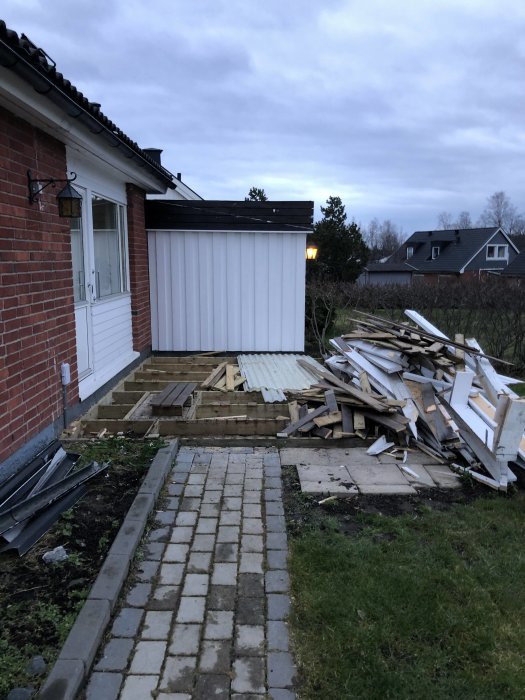 Rivningsmaterial från en altan ligger i en hög bredvid ett hus redo för återvinning.