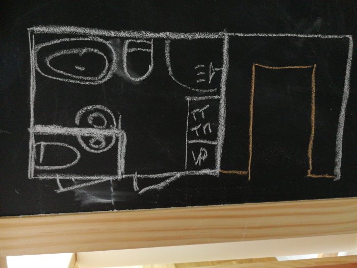 Ritning i krita på svart tavla som föreställer ett U-format kökslayout med markeringar för kyl/frys och dörrar.