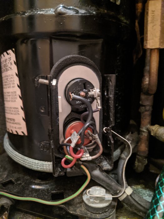 Kompressor med öppet plastlock som visar elektriska anslutningar och en sensor med mörkfärgade sladdar.