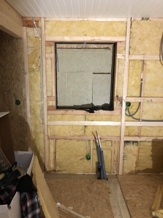 Renoverad vägg med OSB-skivor och isolering, synliga elinstallationer och fönsteröppning under renovering.