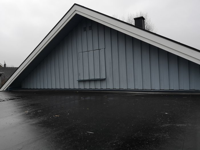 Långsidan av ett hus med ny stående träpanel, takutsprång och en skorsten på taket.