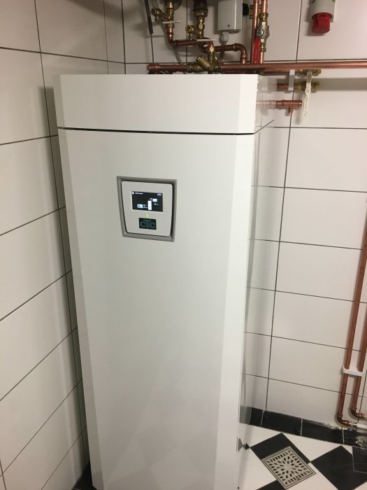 En vit CTC EcoZenith i350L panna med kontrollpanel, omgiven av kopparledningar och vita kakelväggar.