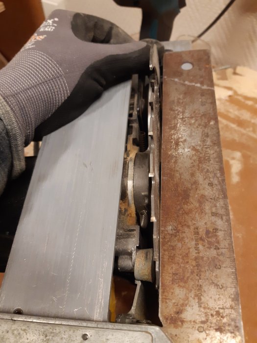Hand i skyddshandske som håller en begagnad cirkelsåg med slitna delar och rostig klinga.