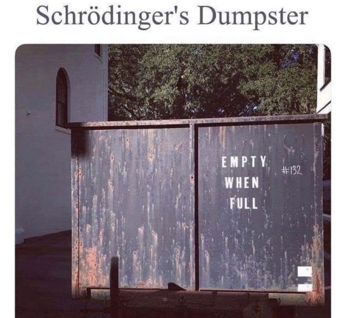 Rostig container med texten "EMPTY WHEN FULL" vid en byggnad, humoristiskt kallad "Schrödinger's Dumpster".