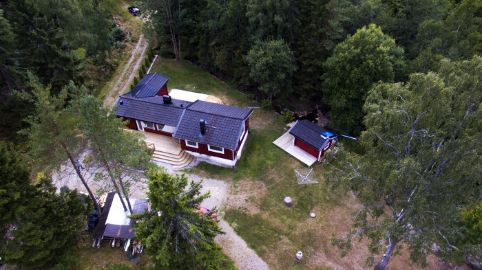 Flygbild över renoverat hus med ny terrass och omlagd fasad omgiven av träd och natur.