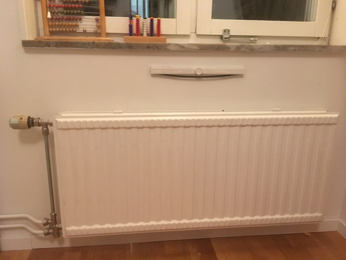 Värmeelement med termostat och vit steglös ventil ovanför i ett rum.