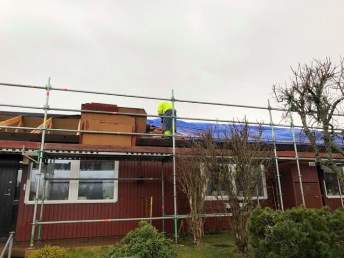 Byggarbetare renoverar taket på ett radhus med borttaget tak och presenningar, risk för vattenskada.