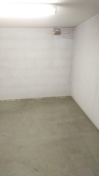 Ett tomt garage med rengjort betonggolv och vita väggar som har sprickor och ett hål efter kabel.