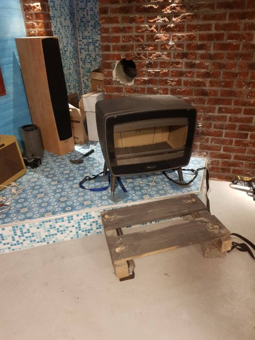 Kamin på pall i renoverat rum med kakel och tegelvägg, förberedd för installation.