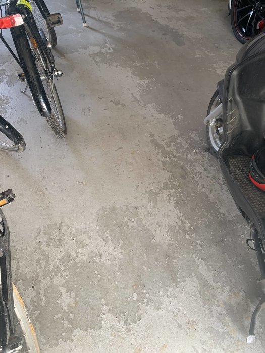 Garagegolv med rester av gammal färg och en parkerad cykel samt del av en skoter.