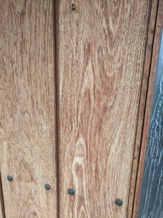 Träpanel med tydlig ådring och mörka skruvar, troligtvis ytterdörr eller fönsterkarm.