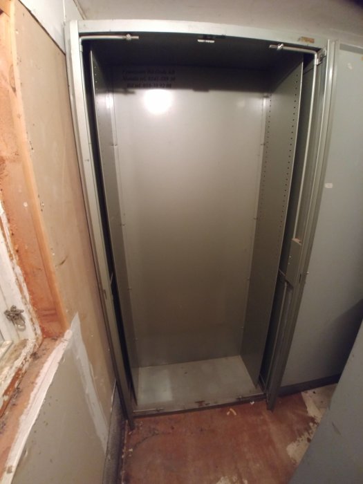 Öppet grått plåtskåp med inåtgående dörrar placerat i ett rum med råa väggar och golv.