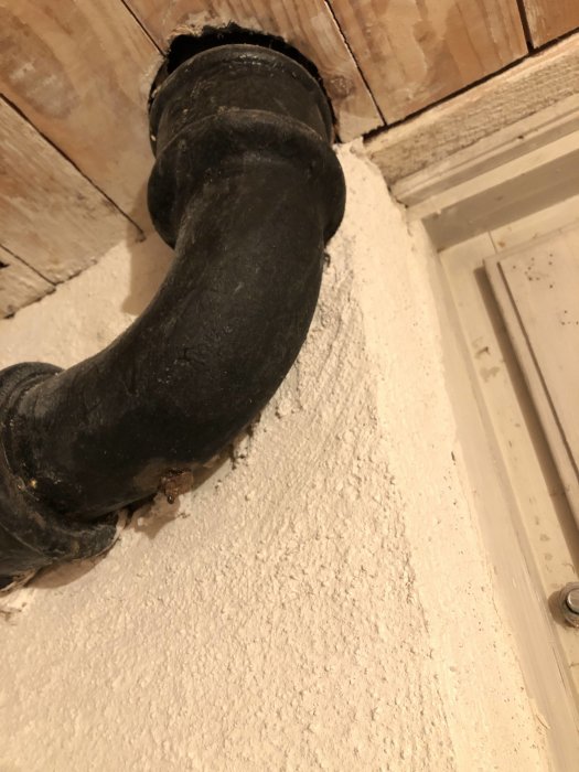Synlig böjd avloppsstam från handfat i källare med en hylla och rostfärg synlig nedanför.