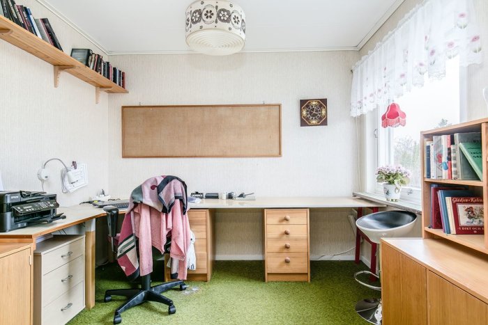 Inrett arbetsrum med gröna heltäckningsmattor, skrivbord, stolar och bokhyllor, utan synlig uppvärmning.