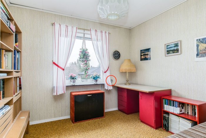 Inrett rum med tapeter, fönster med gardiner, skrivbord och en markerad rund ventilationsöppning vid fönstret.