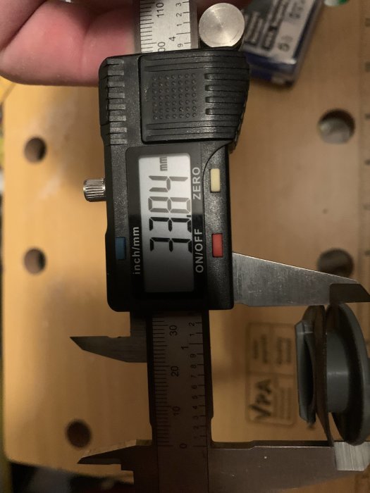 Digital skjutmått visar måttet 21.10 mm på dess display med en trähåld bakgrund.