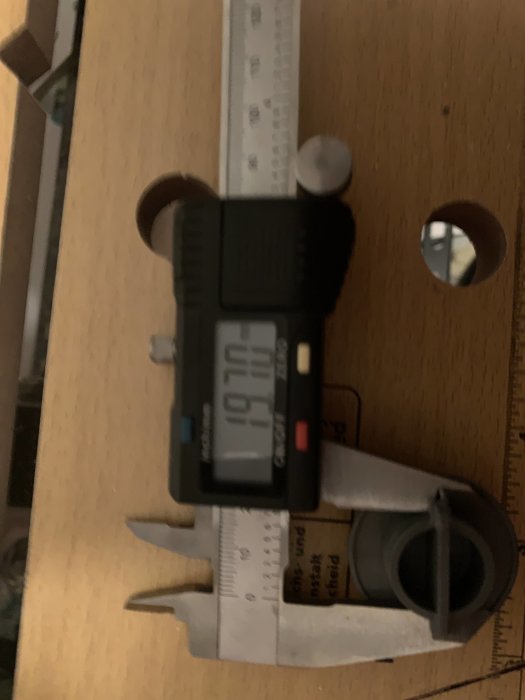 Digital skjutmått som mäter en detalj på en träyta, skärmen visar 20.61.