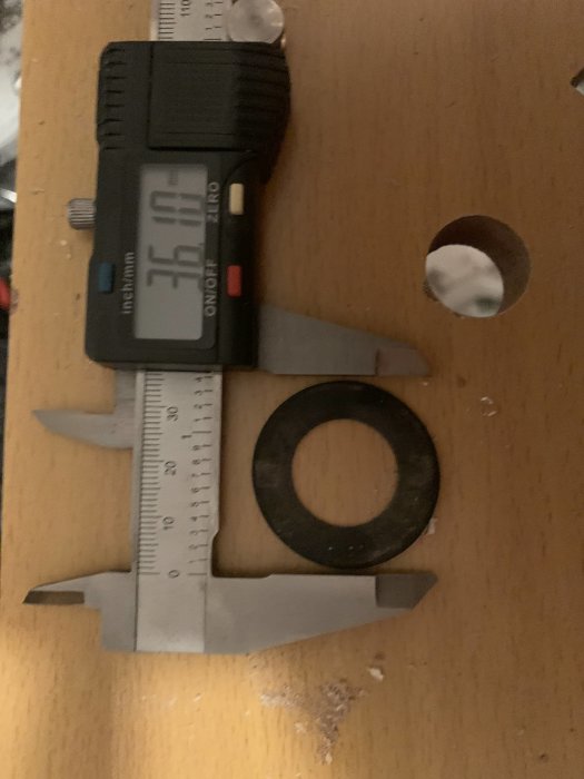 Skjutmått som visar 36 mm bredvid en svart cirkelformad detalj på ett träbord.