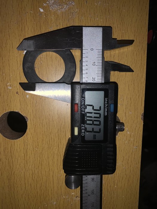 Digital skjutmått mäter en byggdetalj på ett träbord, visar 30.19 mm på displayen.