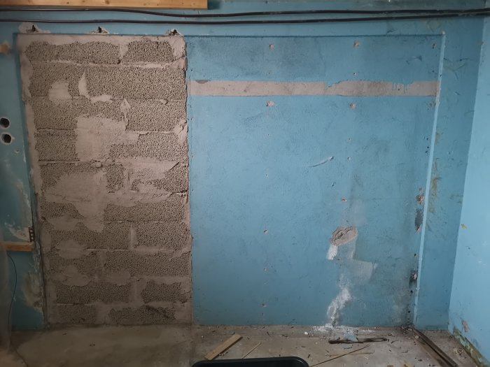Igenmurad tidigare garageport i källarvägg som behöver putsas, avvikande från övrig blå vägg.