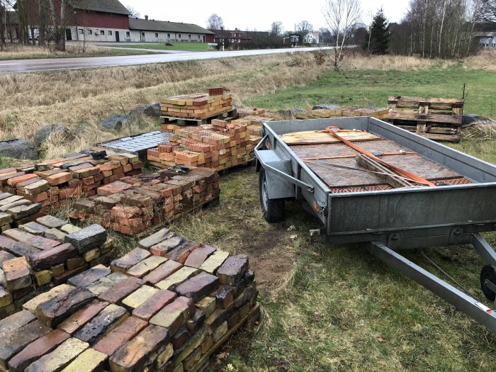 Stapelade tegelstenar bredvid en släpvagn, förberedelse för ett växthusprojekt.