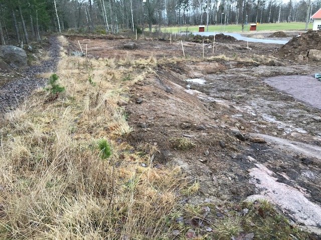 Ojämn slänt med berg och jord, i anläggningsskede, med synliga pinnar som markerar tomtgräns.