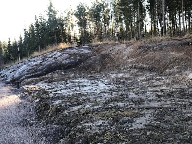 En slänt med en kombination av berg och jord på en tomt, där det finns spår av grus och gräs.