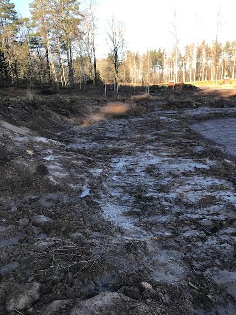 Klurig slänt med berg och jord på en tomt, befintlig grusyta och pinne markerar gräns.