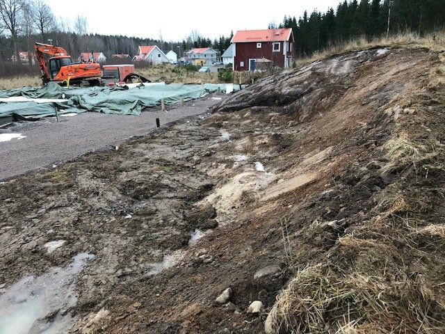 En ojämn slänt med berg och jord vid en byggarbetsplats, med avsikt att förvandlas till en trädgård.