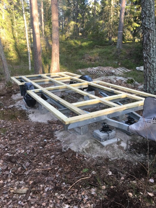 Grundram av tryckade träreglar på betongplintar för pågående byggprojekt i skogsmiljö.