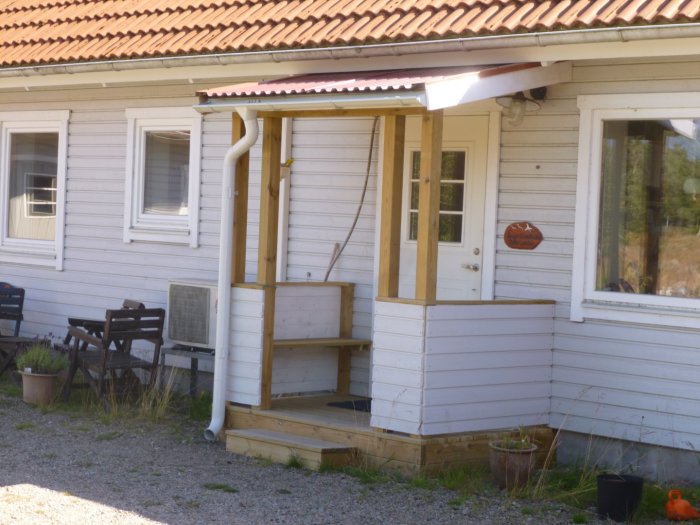 Ett vitmålat trähus med entrétrappa och en skylt som säger "Välkommen till vårt sommarställe".